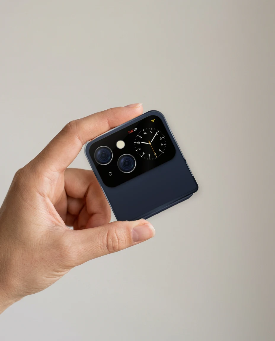 A hand holding iPhone Flip closed in Midnight, the analog Utility watch face on its outer display